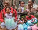 Father hugging his 4-year-old daughter on a backyard swing during her Los Angeles birthday party, while the mother shows her a rabbit to pet.