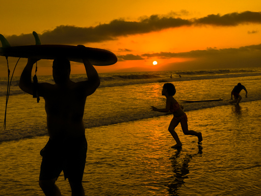 Venice Beach CA - Surfer carries board, boy dances as the sun sinks into the ocean at sunset