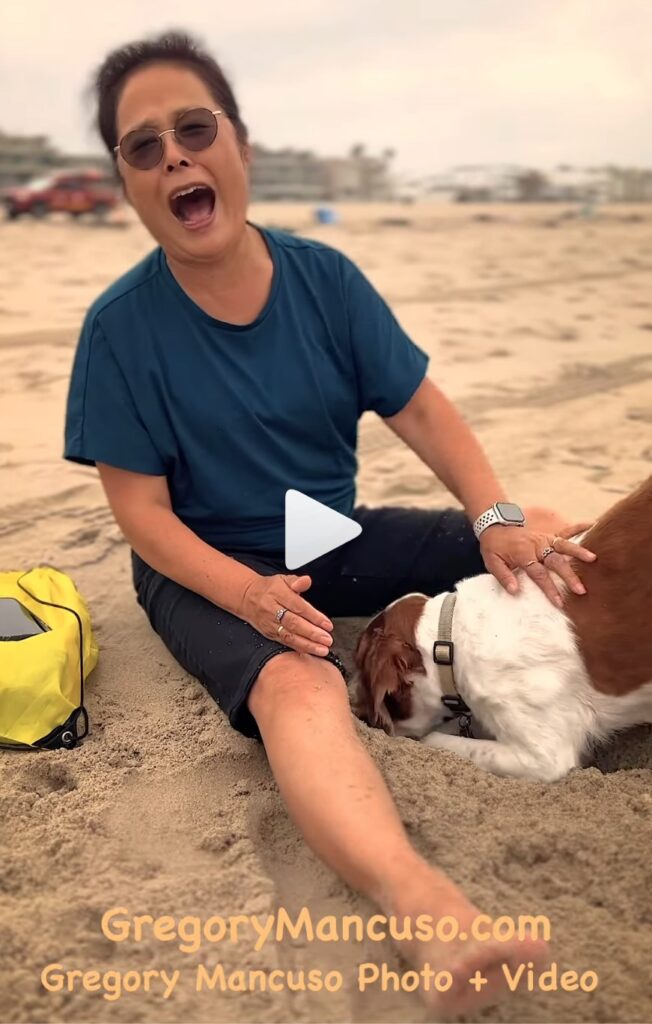 Woman laughing as dog digs hole on beach