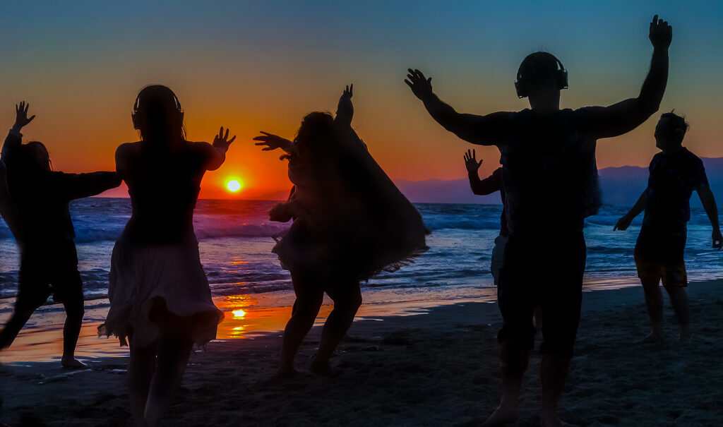 Peoples silhouettes dancing on beach against sunset sky in Los Angeles
